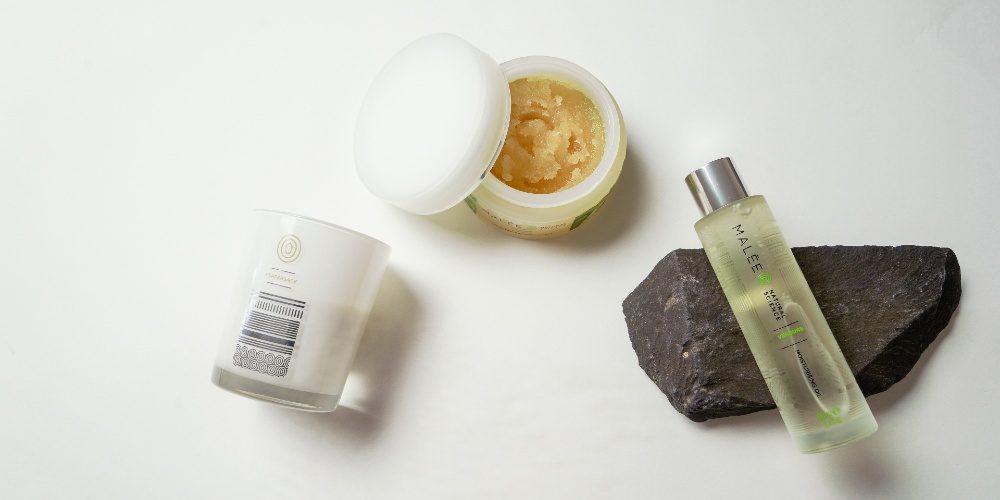 Self-Care Checklist Malee Natural Science With a white background, Malee 100ml Verdure body oil is et on a Dark grey stone, next to it an open 250ml body scrub and a 220ml Peppersage Soy Candle