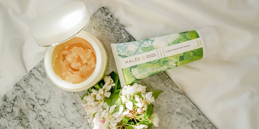 How-to-get-Dye-Off-Skin-Malee-Natural-Science How to get Dye off skin Malee Natural Science. On a marbled table set next to a white linen, an opened 250ml Verdure Body Scrub, 200ml Verdure Conditioning Body Cream and a Jasmin bouquet