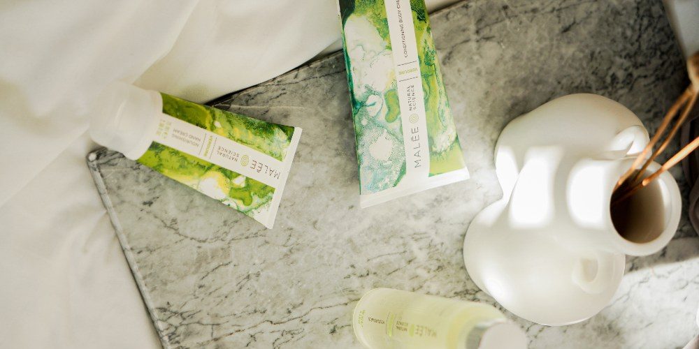 How to get glowing skin Malee Natural Science A marbled tray is set on a white linen, with a white porcelain flower pot Verdure 100ml Moisturising Body Oil, 75ml Nourishing Hand Cream and 200ml Verdure Conditioning Body Cream