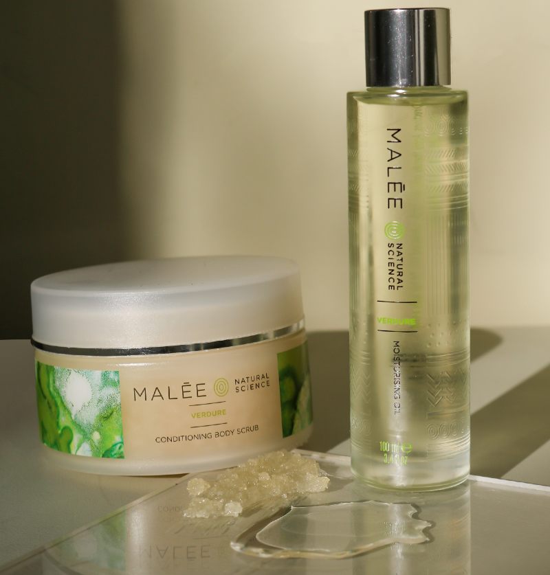 Malée Natural Science Anti pollution skincare ingredients 220g Verdure Conditioning Body Scrub  together with 100ml Verdure Moisturising Oil placed on a table with nude background