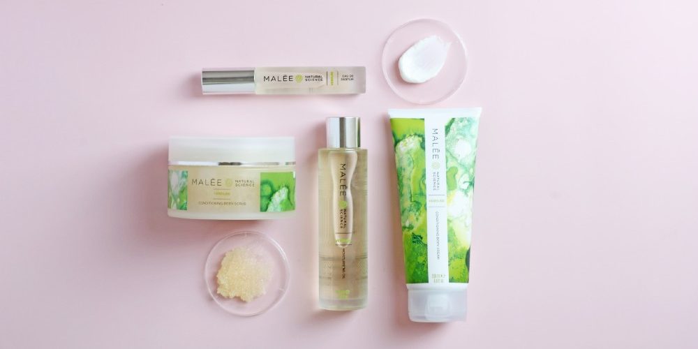 Malée Natural Science How to navigate the body care uk shopping aisles with confidence Malée Natural Science two clear lids one pasted with white body cream and the other one with light brown scrub crystals 200ml Verdure Conditioning Body Cream 220g Verdure Conditioning Body Scrub 100ml Verdure Moisturising Oil Verdure Eau De Parfum all together placed on a pink background