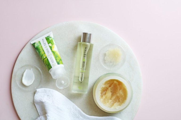 Malée Natural Science75ml Verdure Nourishing Hand Cream 100ml Verdure Moisturising Oil 220g Verdure conditioning Scrub all together placed on a white board close to a white towel with pink background