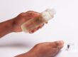 Afro Hair- Malee Natural Science, On a pale pink background, female hands are holding a 100ml Verdure Moisturising oil, with it complete shiny cap next to it.