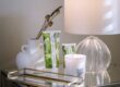 Natural Skincare Tips Malee Natural Science, On a side bed table, the 75ml Verdure Nourishing Hand Cream and the 200ml Verdure Conditioning Body Cream are side by side, with a white ceramic flowers pot, a lighted white sidelight and 220ml Verdure soy candle with a golden little tray