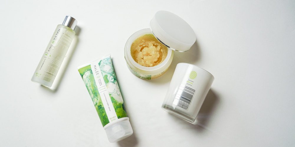 Skincare Ingredients To Avoid Malee natural Science On a white surface, an opened 250ml Malee Moisturising Body scrub, A 100ml Verdure Moisturising Body Oil and a 220ml 100% Verdure Soy Candle
